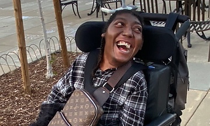 A young woman in her wheelchair laughing outdoors in a town plaza