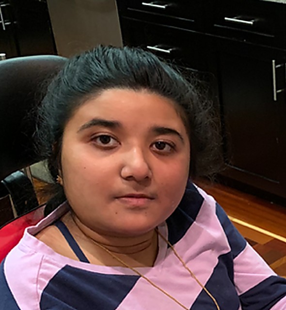 Srinidhi seated in her wheelchair at home, looking directly at the camera